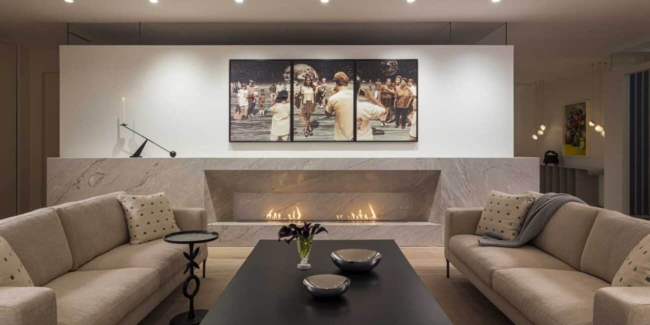 Striking yet calming in its innovative design, the living room features a custom 19-foot BioFlame soft stone fireplace that leaves a blank backdrop for Yoshio Itagaki’s Tourists on the Moon #2, 1998, above. Graphic black furnishings that balance the mood are an ebony-stained white oak drum coffee table designed by Iman and fabricated by Peter Kohl; an Interconnect Candle Holder, designed by Colin King for Audo Copenhagen on the mantle; and a Corbin Bronze XO Table.