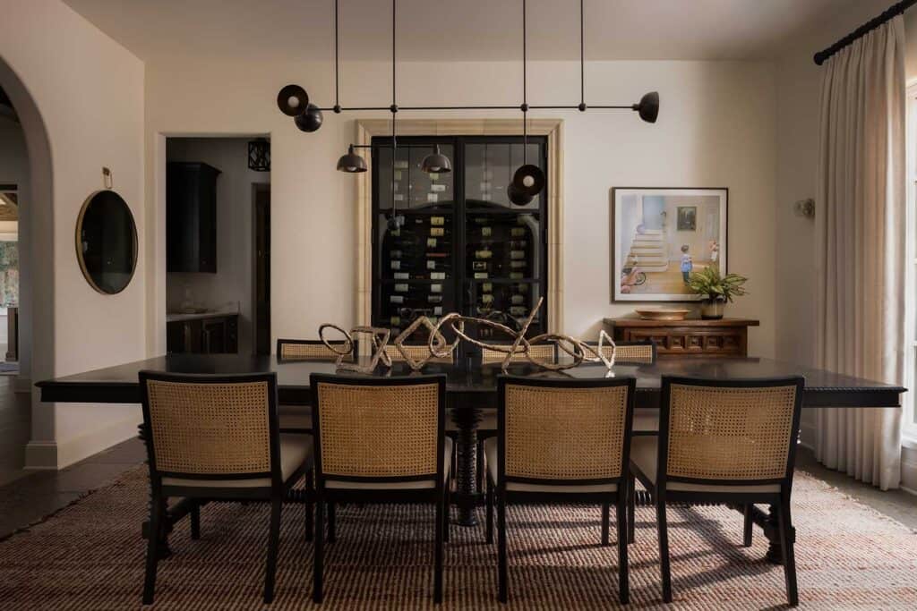 In the dining room, a wine cellar behind glass with a stone surround existed, so the designers chose to make it a special, if not convenient, focal point of the space. To the right is a photograph by Julie Blackmon. The ceiling light fixture by Apparatus hangs over a trio of Tom Corbin sculptures, adding a playful note to the elegant turned-leg table by Alfonso Marina, with 18th-century Portuguese influence.