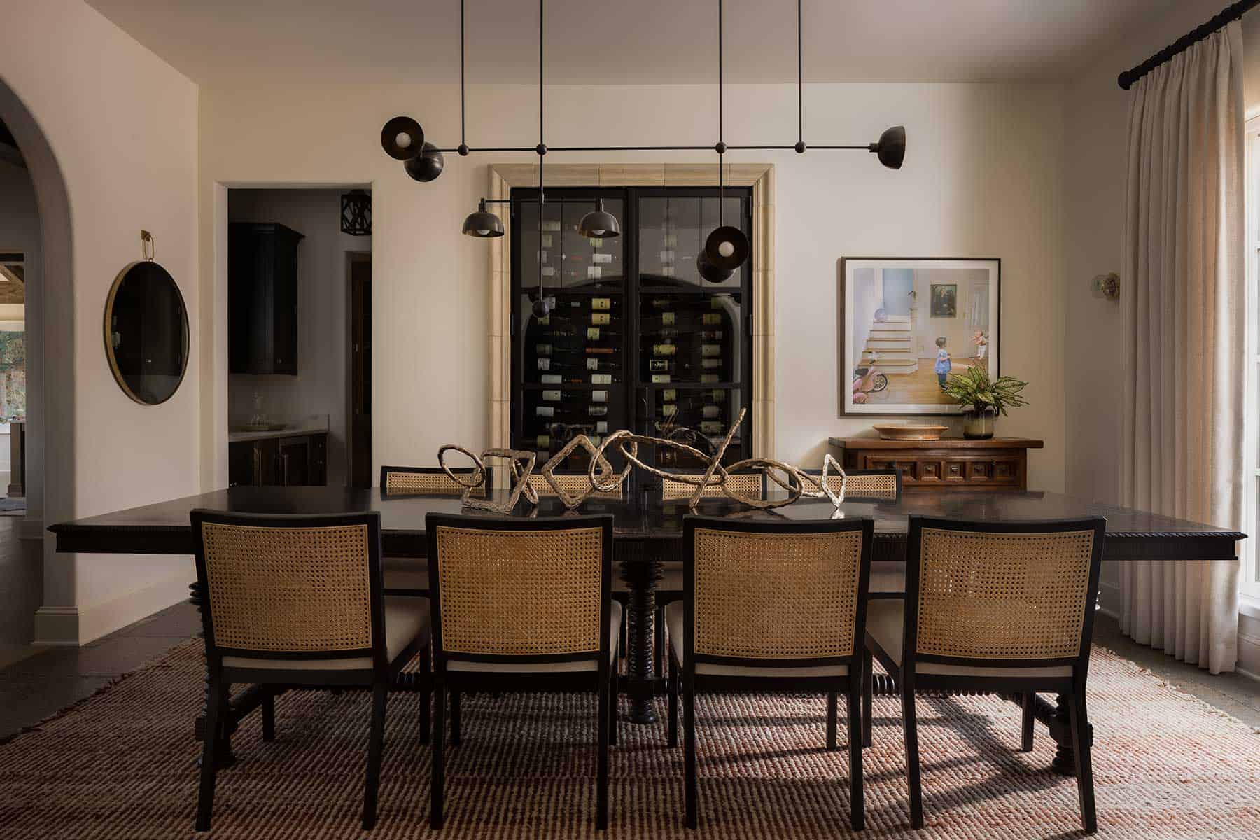 In the dining room, a wine cellar behind glass with a stone surround existed, so the designers chose to make it a special, if not convenient, focal point of the space. To the right is a photograph by Julie Blackmon. The ceiling light fixture by Apparatus hangs over a trio of Tom Corbin sculptures, adding a playful note to the elegant turned-leg table by Alfonso Marina, with 18th-century Portuguese influence.